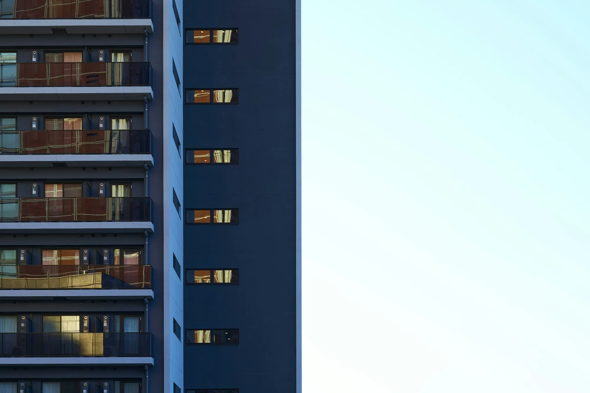 Façade contemporaine aux fenêtres allumées une à une : chaque logement joignable devient une adresse de plus dans une liste parcourue sans relâche