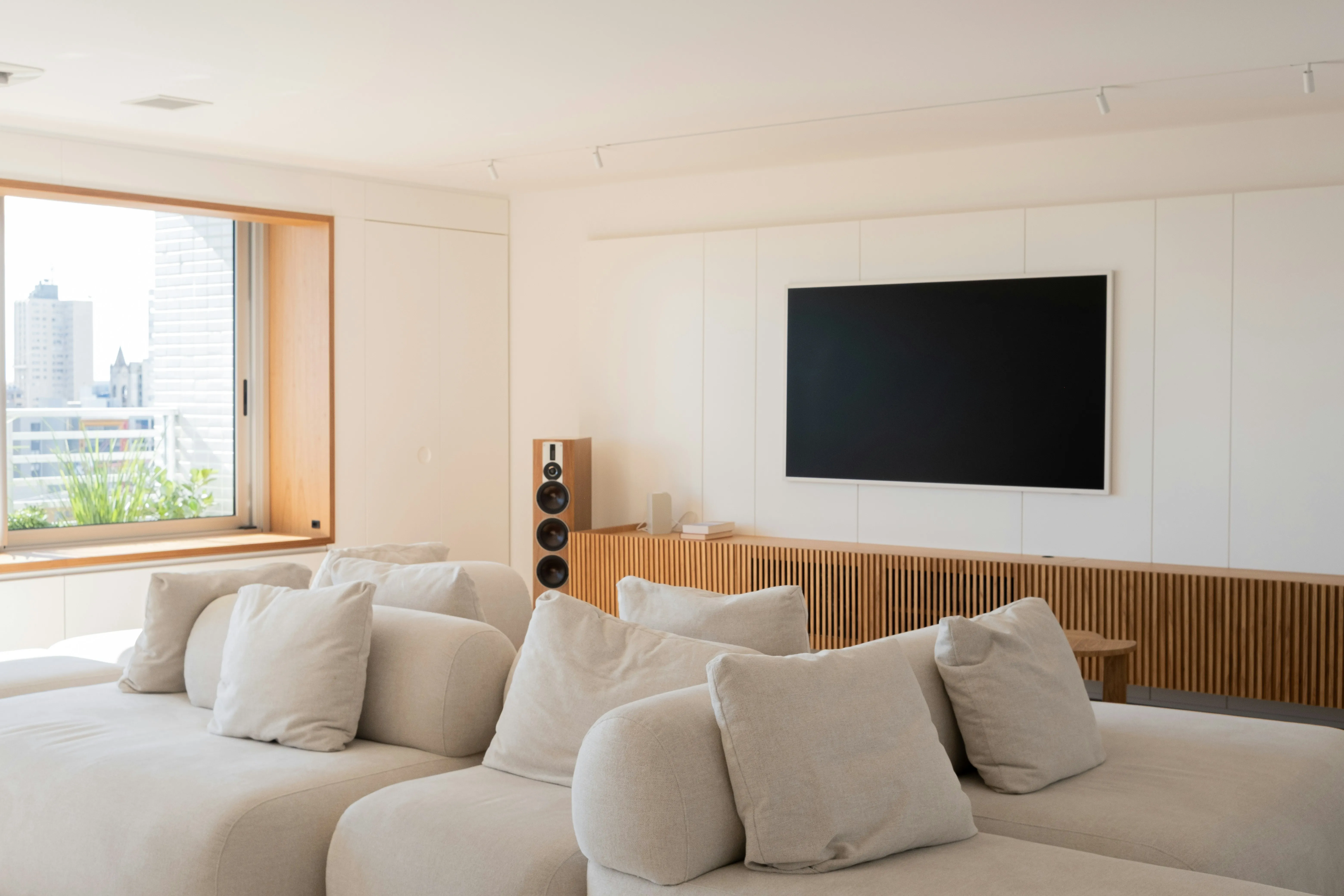 Salon épuré avec écran encastré et enceinte colonne en bois, façade urbaine en arrière-plan : le niveau de finition que revendiquent aussi bien Loxone que les intégrateurs Home Assistant les plus soignés