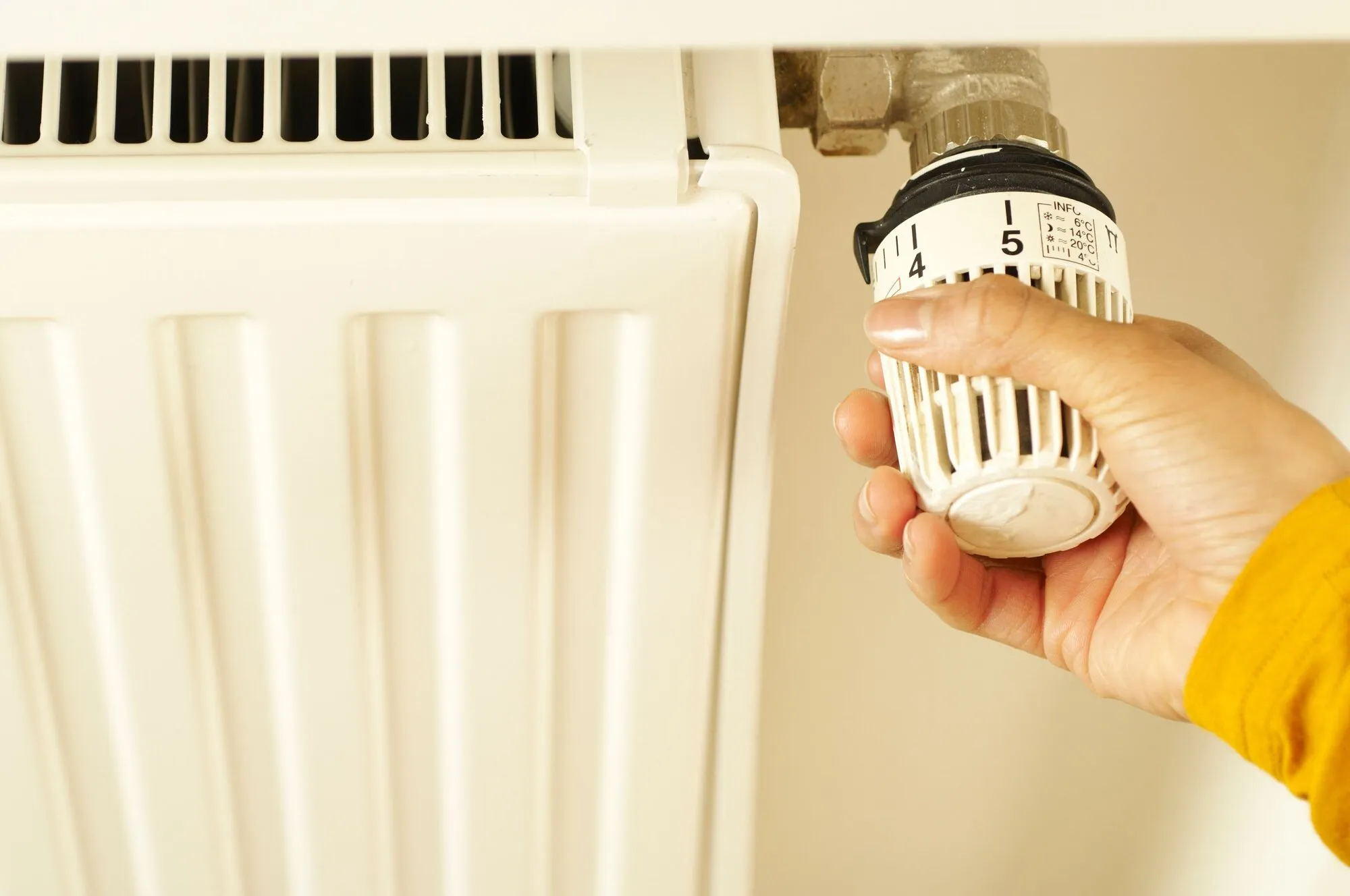 Main réglant une tête thermostatique graduée sur un radiateur : le genre de consigne qu’on règle en partant, et qu’on ne regarde plus pendant des semaines