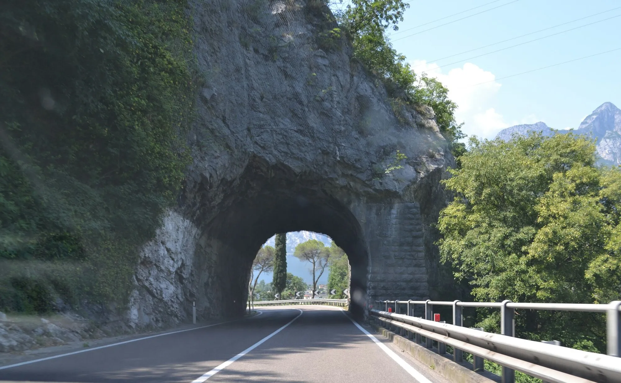 Route qui traverse la roche vers la lumière, lac et montagnes au bout : le tunnel privé relie deux points sans rien ouvrir sur le chemin